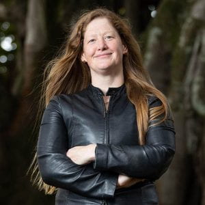Nicola Gaston smiles at the camera in a leather jacket with her arms folded.